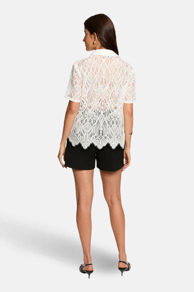 Short noir de Morgan de Toi, porté avec un chemisier en dentelle blanche et des talons aiguilles.