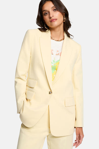 Blazer jaune de Morgan de Toi porté sur un t-shirt imprimé, avec collier et boucles d'oreilles dorées.