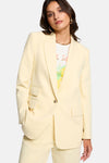 Blazer jaune de Morgan de Toi porté sur un t-shirt imprimé, avec collier et boucles d'oreilles dorées.