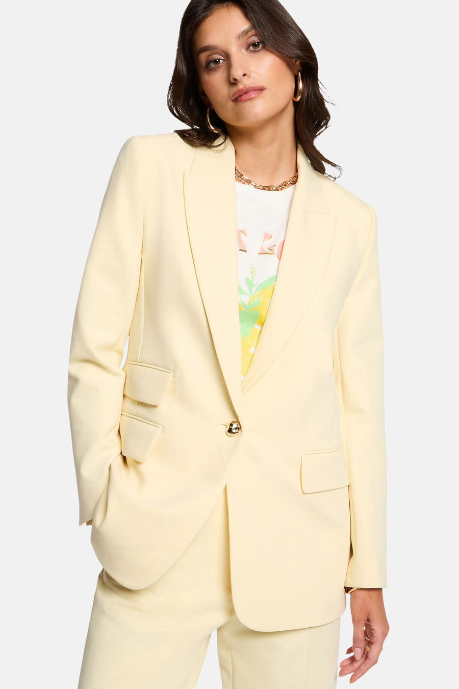 Blazer jaune de Morgan de Toi porté sur un t-shirt imprimé, avec collier et boucles d'oreilles dorées.