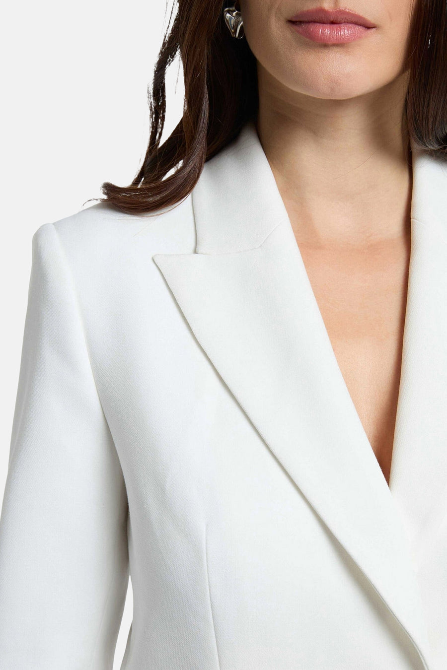 Blazer blanc de Morgan de Toi, porté par une femme aux cheveux bruns avec un décolleté plongeant et une boucle d'oreille argentée.