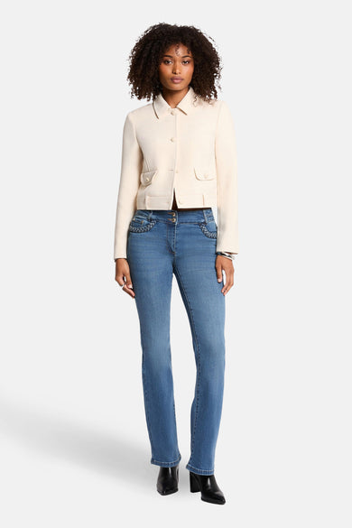 Korte ecru jas van Morgan de Toi, met omgeslagen kraag en opgestikte zakken, gedragen met een blauwe jeans en zwarte enkellaarsjes.