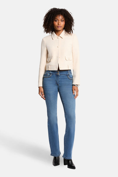Korte ecru jas van Morgan de Toi, met omgeslagen kraag en opgestikte zakken, gedragen met een blauwe jeans en zwarte enkellaarsjes.