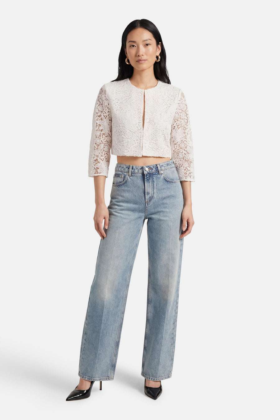 Gilet blanc en dentelle de Morgan de Toi, avec manches trois-quarts, porté avec un jean bleu taille haute et des escarpins noirs.
