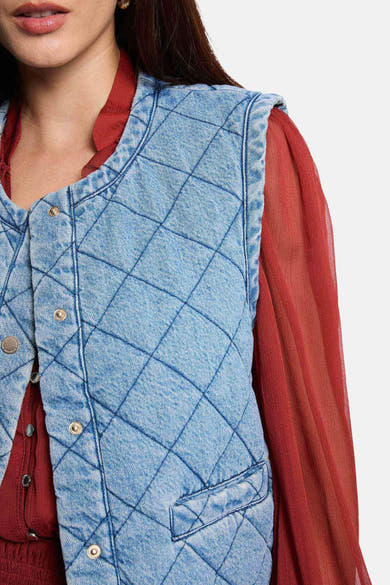 Veste sans manches en denim bleu clair de Morgan de Toi, matelassée à carreaux, portée sur un chemisier bordeaux.
