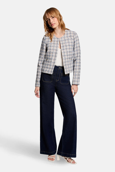 Veste courte bleue en tweed par Morgan de Toi, à motif à carreaux, portée avec un pantalon foncé et des sandales blanches.