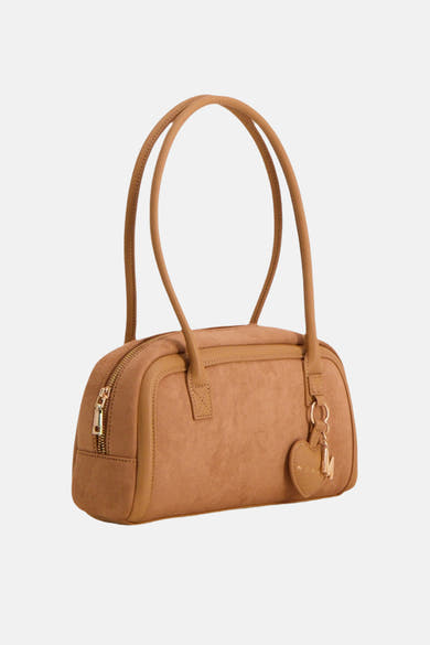 Cognac suede handbag with rounded shape and dual top handles, featuring a side zipper and heart-shaped charm with initial detail, front view