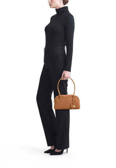 Cognac leather handbag with rounded top handles and heart-shaped charm, side view on model in black outfit