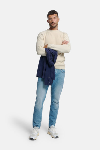 Pull ras du cou écru de NO EXCESS, porté avec un jean bleu clair et une chemise bleu marine pliée.

