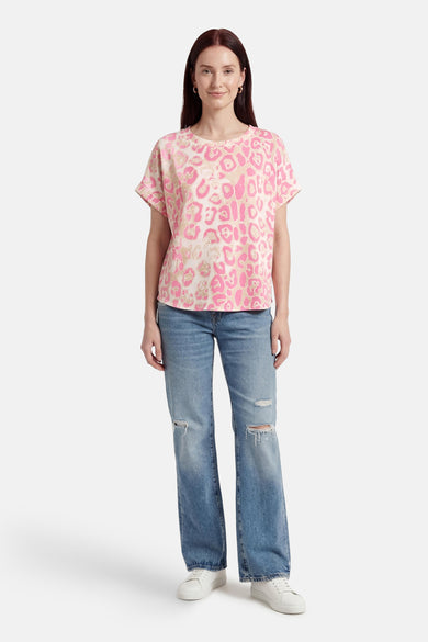 T-shirt rose à manches courtes de Terra di Siena avec un motif léopard, porté avec un jean bleu délavé et des baskets blanches.