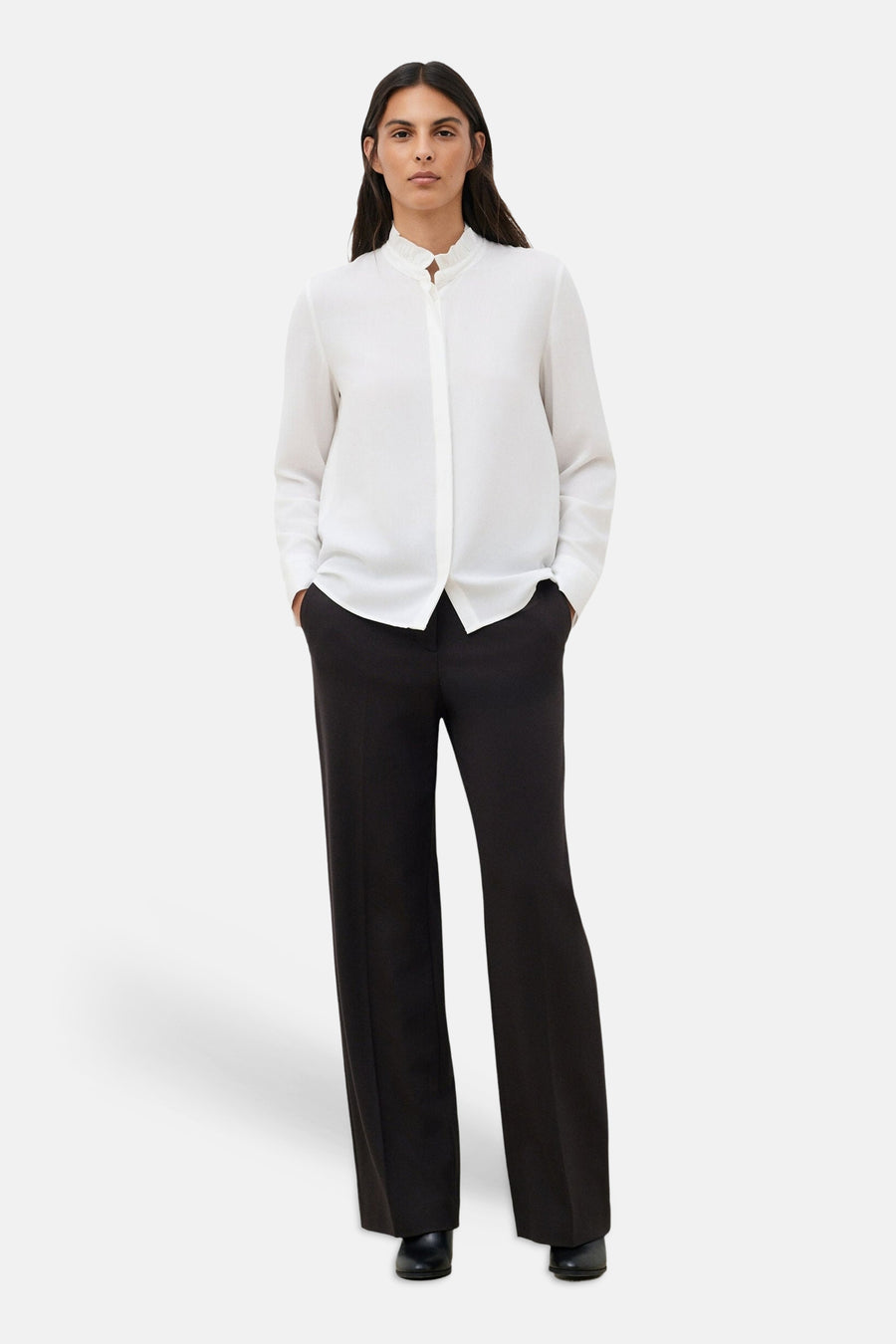 White long-sleeve blouse with ruffled stand collar by CAROLL, worn with black wide-leg trousers and black shoes, front view