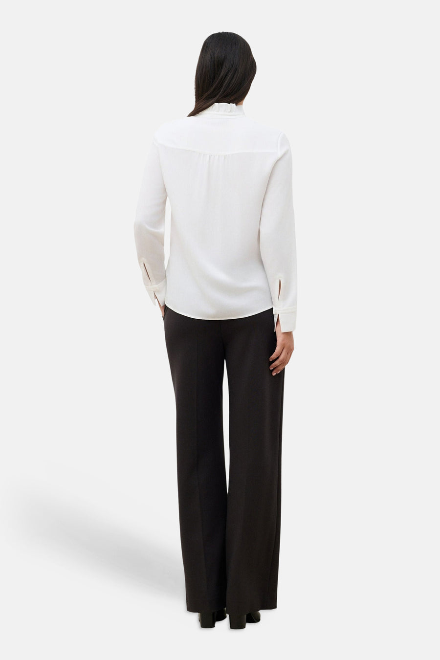 White long-sleeve blouse by CAROLL, back view, featuring ruffled collar and sleeve slits, paired with black trousers.