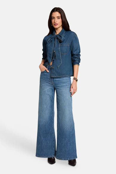 Mid blue denim long-sleeve blouse with front bow and chest pocket, worn with matching flared jeans and black boots, full-length front view