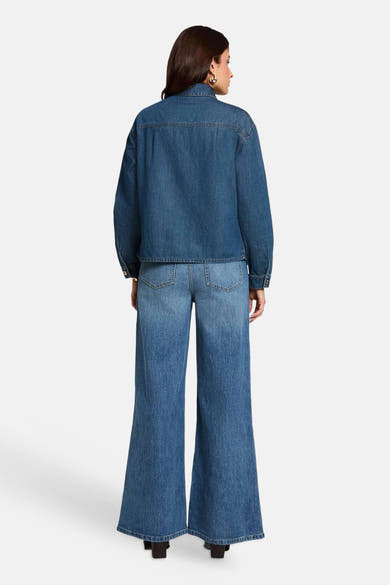 Mid blue denim long-sleeve shirt from back view, featuring classic collar and buttoned cuffs, paired with matching wide-leg jeans.