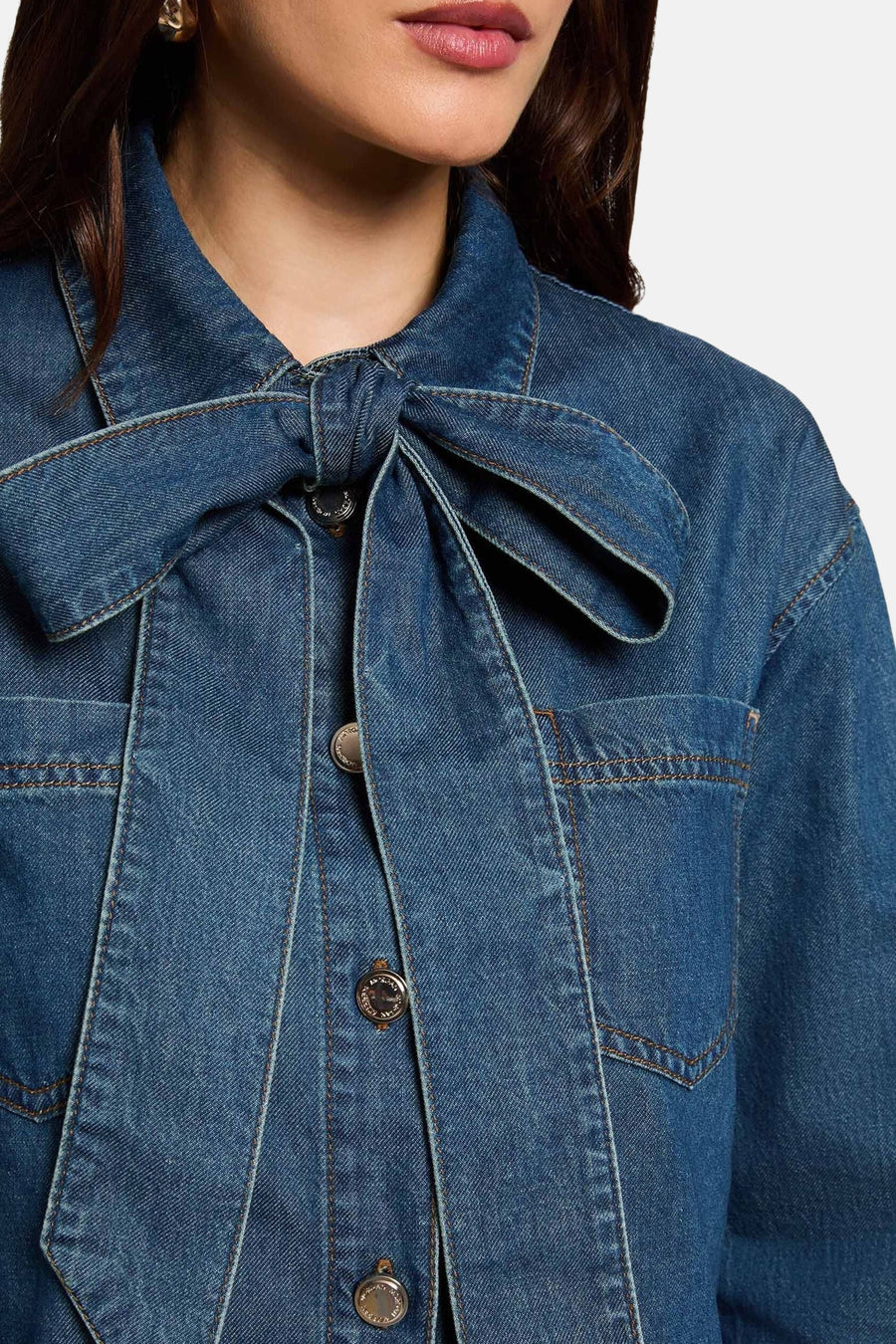 Mid blue denim long-sleeve blouse with front tie bow and button closure, cropped close-up view