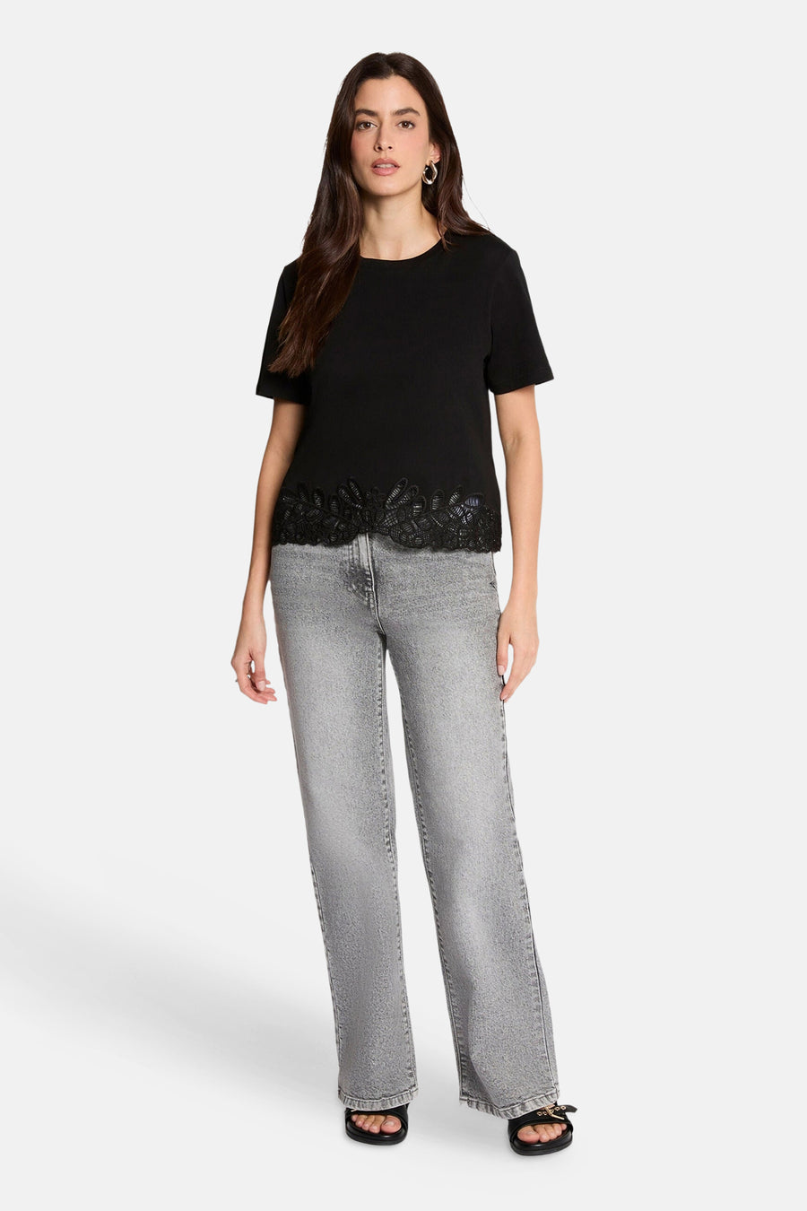 Black short-sleeve t-shirt with lace trim hem, worn with light gray jeans and black sandals, front view.