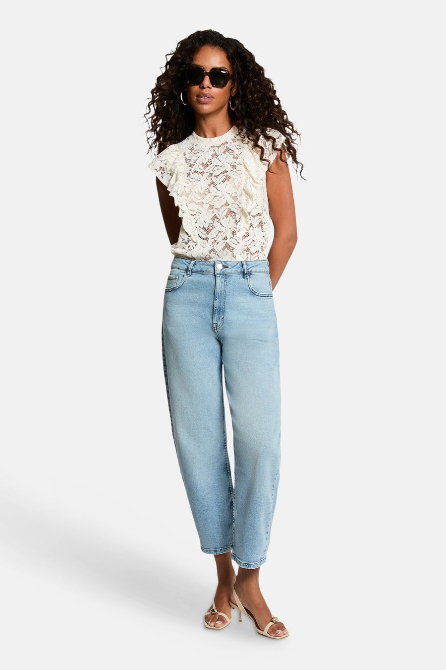 Ecru lace short-sleeve blouse with ruffled cap sleeves, worn with light blue jeans and strappy heels, full-body lifestyle view