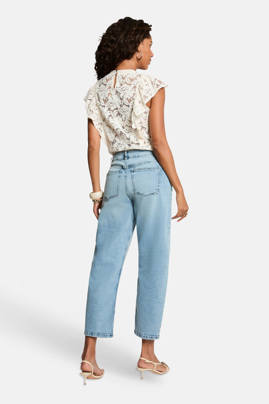 Ecru lace short-sleeve blouse with ruffled cap sleeves and back keyhole, shown from back view on model wearing light blue jeans and strappy heels