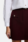 Burgundy textured mini skirt with front pocket and gold-tone button, side view, paired with white blouse