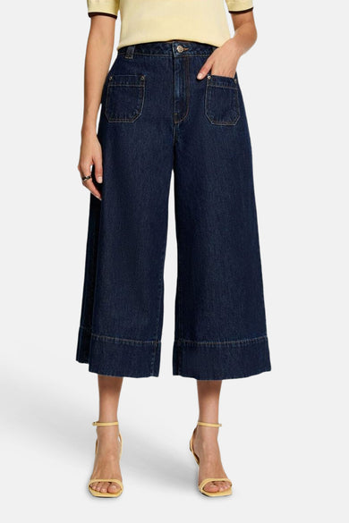 Dark blue wide-leg denim culottes by PIKILO, featuring front pockets and cuffed hems, shown on model with yellow top and sandals.