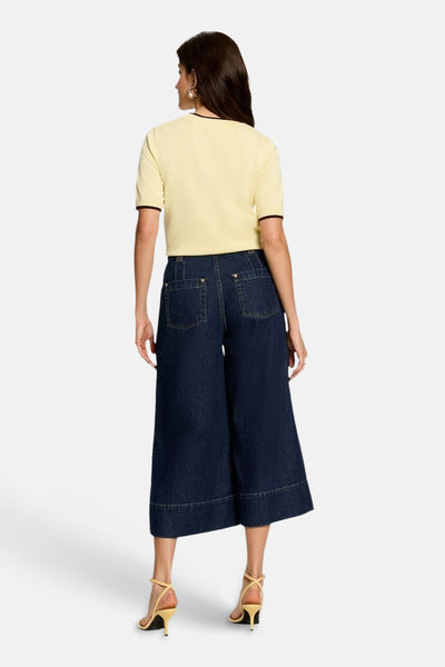 Dark blue wide-leg denim jeans by PIKILO, back view, cropped length with cuffed hems and classic back pockets, worn with a yellow top and strappy heels.