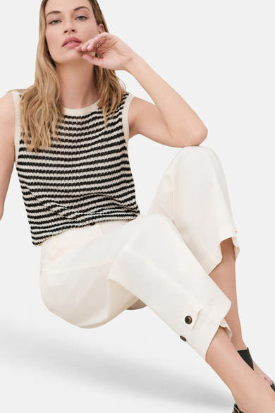Beige wide-leg trousers with buttoned cuffs, worn with a striped knit top and black heels, side view lifestyle shot