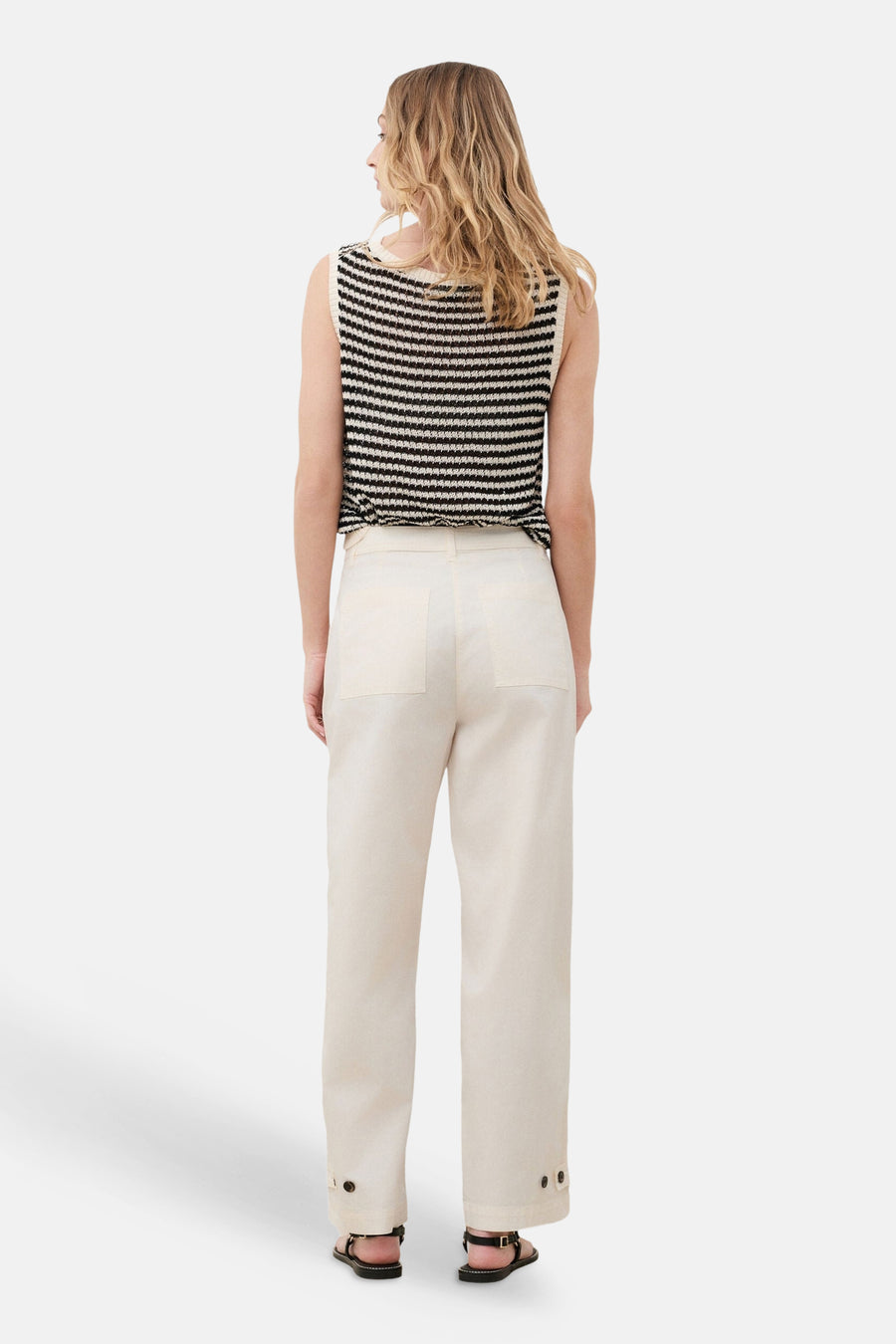 Beige straight-leg trousers with buttoned cuffs and back pockets, shown from the back on a model wearing a striped top and sandals.