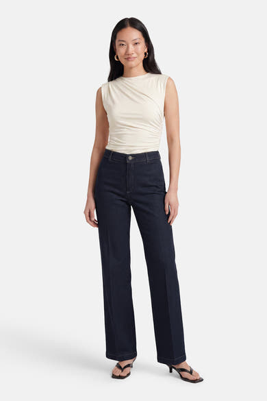 Dark blue wide-leg denim jeans by MIRA, high-rise fit with clean stitching, worn with cream sleeveless top and black heels, full-length front view