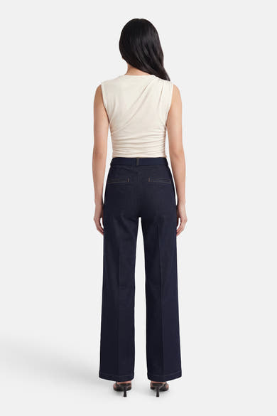Dark blue wide-leg denim jeans by MIRA, back view, featuring clean stitching and structured fit, worn with cream top and heels.