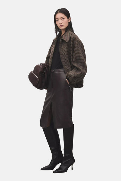 Black long-sleeve t-shirt by model wearing houndstooth jacket, leather skirt, and knee-high boots in lifestyle side view