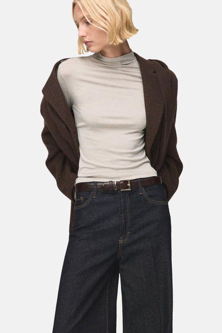 T-shirt beige à manches longues de MANGO, porté avec une veste marron à motifs et un pantalon taille haute bleu marine.