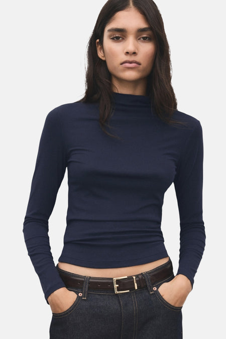 T-shirt bleu à manches longues de MANGO, porté avec un jean taille basse et une ceinture en cuir marron.
