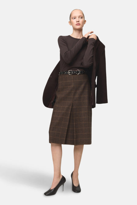 T-shirt à manches longues brun de MANGO, porté avec une jupe à carreaux et des talons noirs.