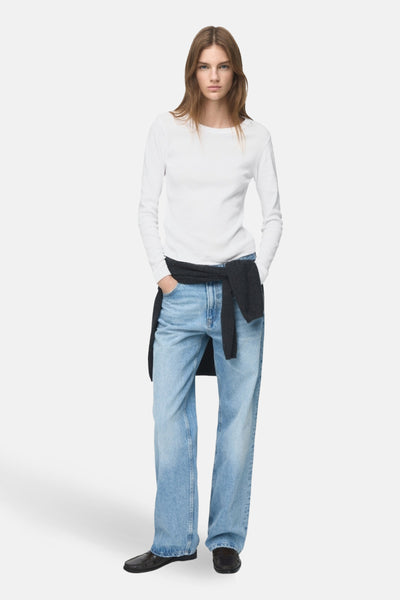 T-shirt à manches longues blanc de MANGO, porté avec un jean bleu et un pull noué à la taille.