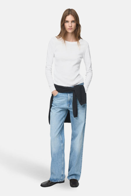 T-shirt à manches longues blanc de MANGO, porté avec un jean bleu et un pull noué à la taille.