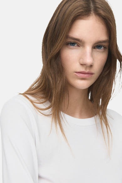 T-shirt à manches longues blanc de MANGO, porté par une femme aux cheveux longs et ondulés.