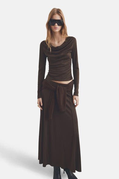 T-shirt à manches longues brun de MANGO, avec un drapé au niveau du cou, porté avec une jupe longue.
