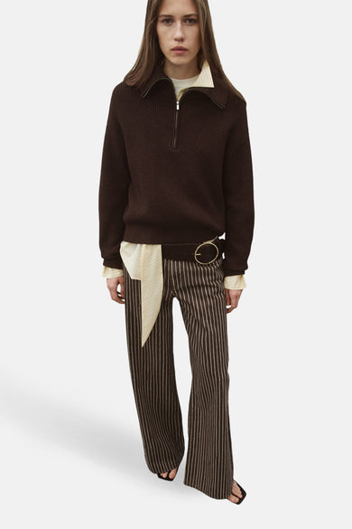 Jean coloré brun de MANGO, à rayures verticales, porté avec un pull et une ceinture.
