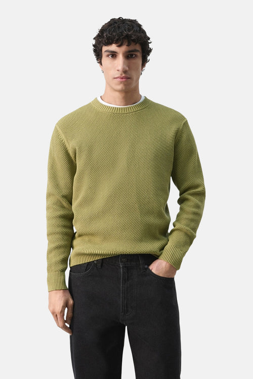 Pull à col rond vert par MANGO, texture tricotée en maille gaufrée, porté sur un t-shirt blanc et un jean noir.
