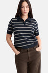 Polo à manches courtes bleu par MANGO, à rayures blanches horizontales porté avec un pantalon marron.
