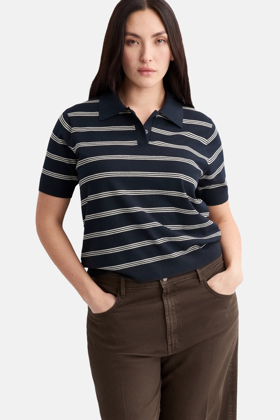 Polo à manches courtes bleu par MANGO, à rayures blanches horizontales porté avec un pantalon marron.

