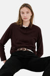 Pull col rond bordeaux par MANGO, porté avec un pantalon noir et une ceinture marron.