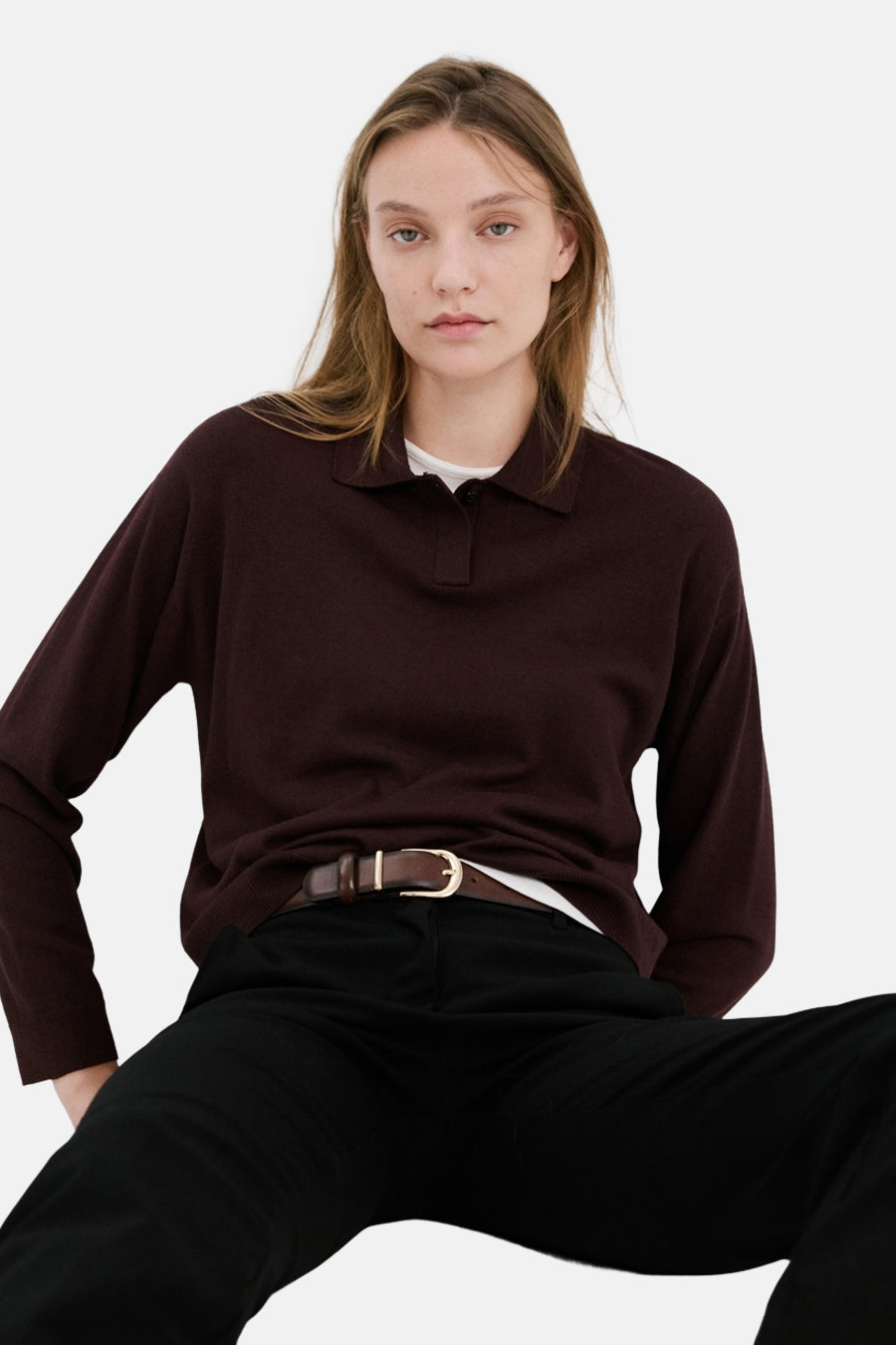 Pull col rond bordeaux par MANGO, porté avec un pantalon noir et une ceinture marron.