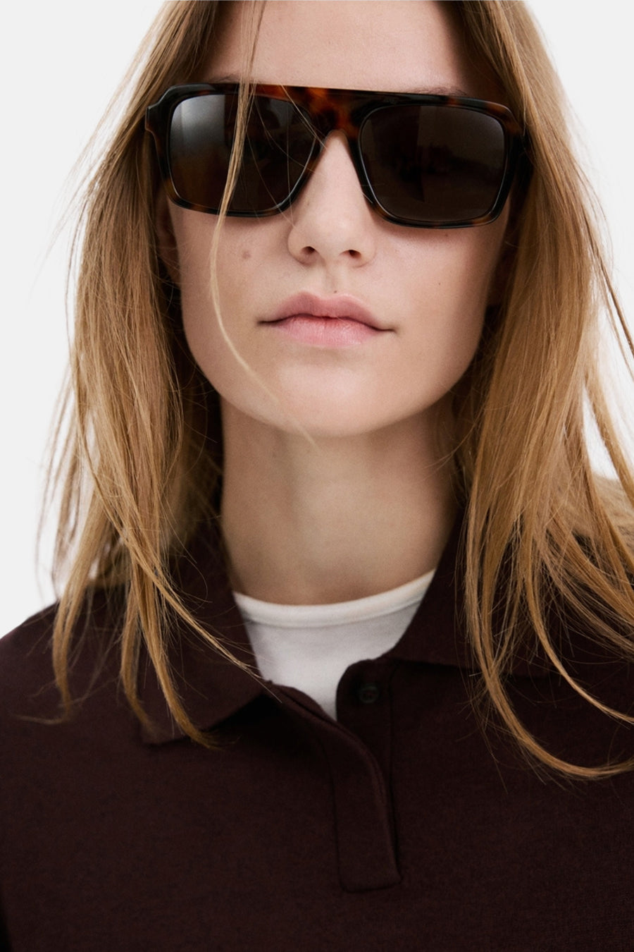 Pull col rond bordeaux de MANGO, porté avec une chemise blanche et des lunettes de soleil écaille de tortue.