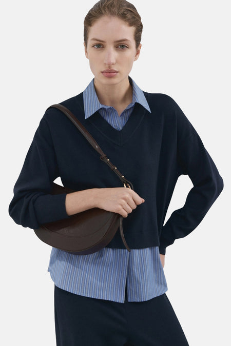 Pull col V bleu de MANGO, porté sur une chemise rayée bleu clair, avec un pantalon bleu marine.