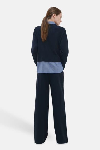 Pull col V bleu par MANGO, porté avec une chemise rayée et un pantalon large assorti, vue de dos.
