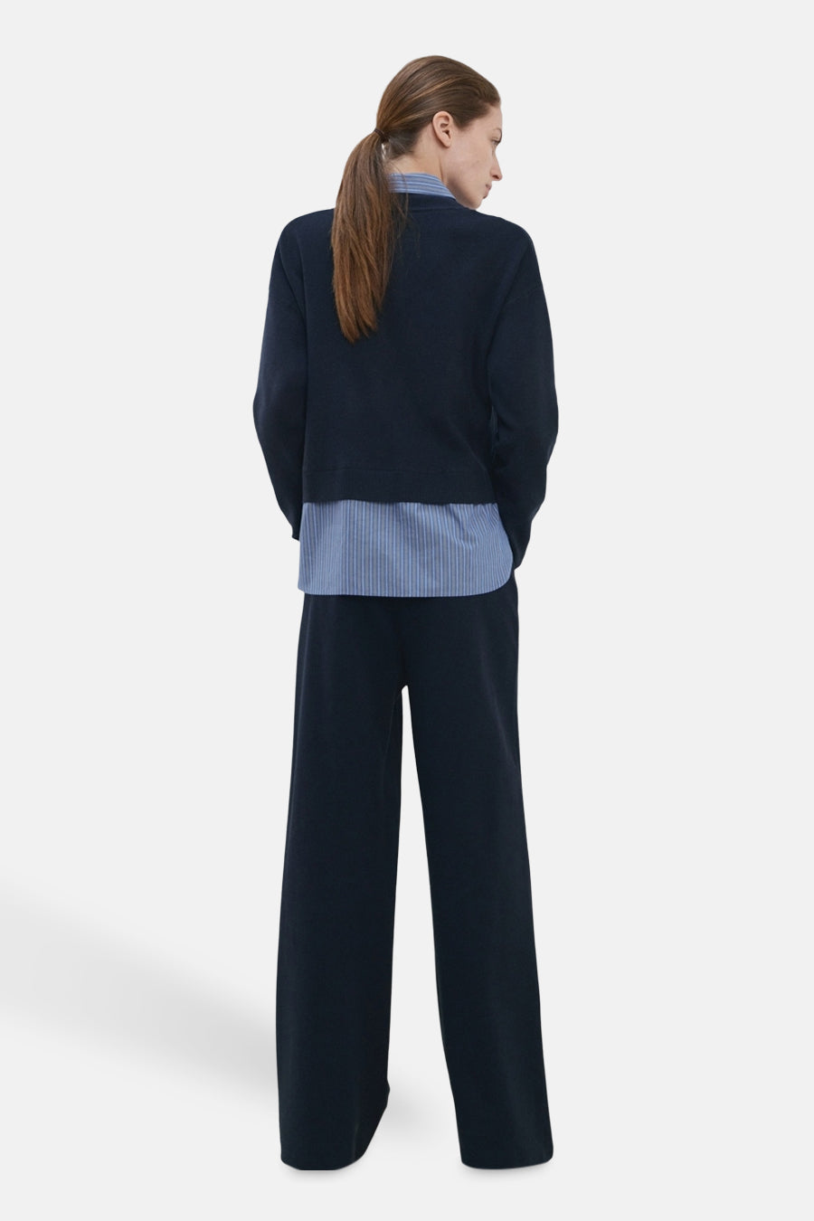 Pull col V bleu par MANGO, porté avec une chemise rayée et un pantalon large assorti, vue de dos.
