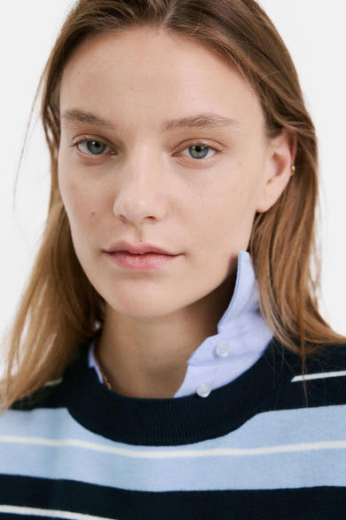 Pull ras du cou multicolore de MANGO avec des rayures horizontales, porté avec une chemise bleu clair.