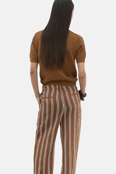 Polo brun de MANGO, manches courtes et texture ajourée, porté avec un pantalon rayé marron et blanc, vue de dos.