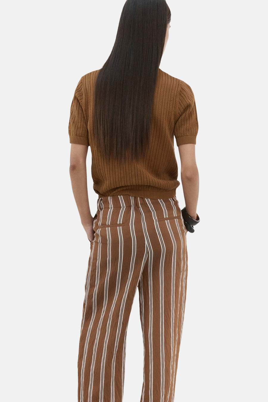 Polo brun de MANGO, manches courtes et texture ajourée, porté avec un pantalon rayé marron et blanc, vue de dos.